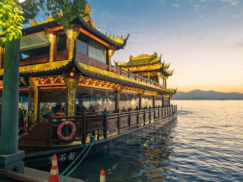 Hangzhou, China - November 29, 2025: Traditional Chinese pleasure boat adorned with golden details illuminated at sunset on a scenic lake