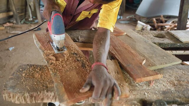 Wideangle black woodworker cutting plank with jigsaw, sawdust plume and hands guiding tool over rough bench dynamic motion, measurement marks, industrious energy in busy workshop