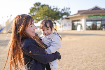 Fototapeta premium Warm sunlight bathes a mother and child. Mother smiles gently, holding her young daughter close. Child gazes downward, peaceful and content