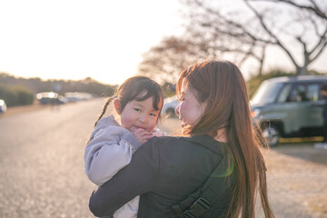Fototapeta premium Warm sunlight bathes a tender embrace between mother and child. Child smiles softly, eyes bright with delight and affection. Mother's face glows with gentle joy, arms cradling the small one