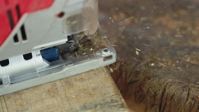 Dynamic jigsaw trimming pallet edge, red tool housing, fast chip ejection and fine shavings flying, closeup blade contact with coarse grain, reveal of wooden dowel and trimmed edge, energized workshop