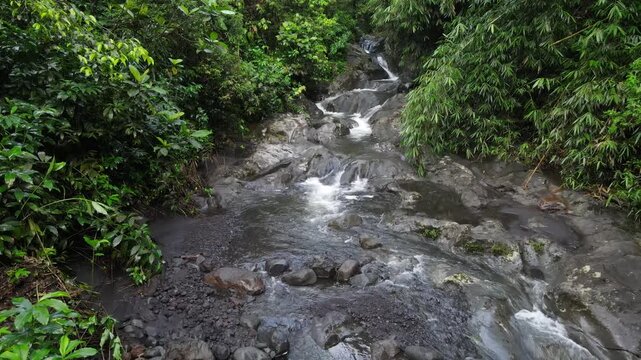 Aerial view of Small waterfall cascading over smooth stones in a tropical jungle, Clear mountain stream running through a rocky riverbed. babbling brook and vibrant green foliage.