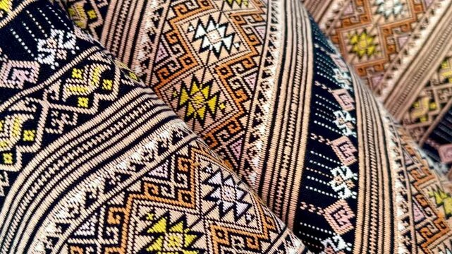A panning close-up of traditional Thai hand-woven fabrics featuring intricate geometric patterns and earth-tone colors, showcasing the texture, weaving craftsmanship, and cultural details.