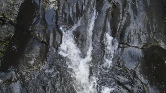 Aerial view of Small waterfall cascading over smooth stones in a tropical jungle, Clear mountain stream running through a rocky riverbed. babbling brook and vibrant green foliage.