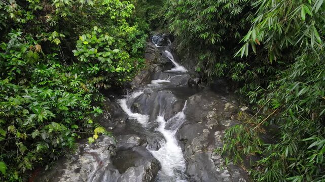 Aerial view of Small waterfall cascading over smooth stones in a tropical jungle, Clear mountain stream running through a rocky riverbed. babbling brook and vibrant green foliage.