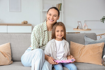 Fototapeta premium Happy young woman and her daughter with cosmetics for kids on sofa in living room