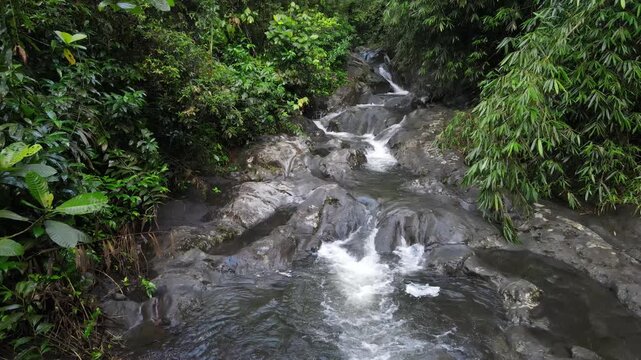Aerial view of Small waterfall cascading over smooth stones in a tropical jungle, Clear mountain stream running through a rocky riverbed. babbling brook and vibrant green foliage.