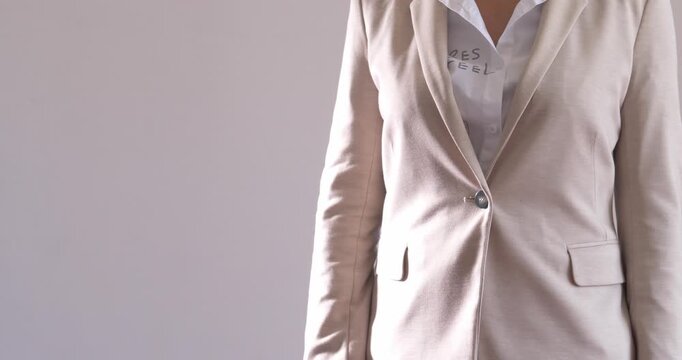 A modern young woman in a business suit stands on a light background and shows a gesture of touching the touchscreen