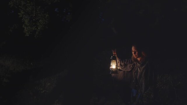 A woman with a kerosene lamp walks through a dark forest