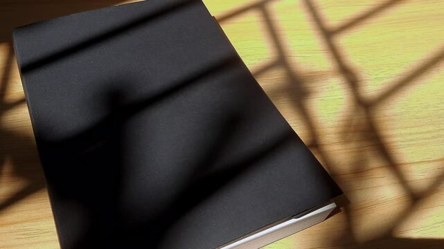 Black Notebook On Wooden Desk Under Warm Afternoon Sunlight And Soft Leaf Shadows