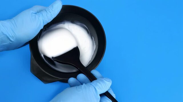 Professional colorist preparing hair coloring cream in a mixing bowl with a brush