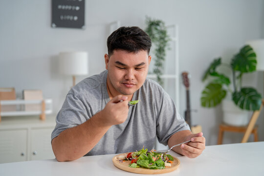 Asian young plus-size man enjoy eating favorite healthy salad in house.
