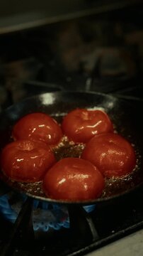 Close-up of tomatoes sizzling in a frying pan over gas flame. Hot oil bubbling and cooking process in a professional kitchen.