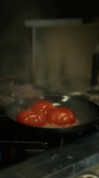 Whole tomatoes hitting a hot pan with a burst of flame. Professional kitchen cooking, high heat saut&eacute;ing and dramatic culinary action.