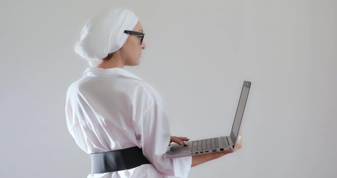 Business goal-oriented young woman in glasses and a turban with a laptop in her hands at work. View from the back.
