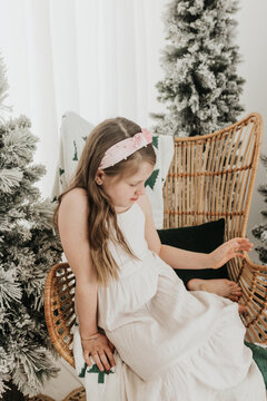 Young girl smiles while posing in chair surrounded by flocked trees
