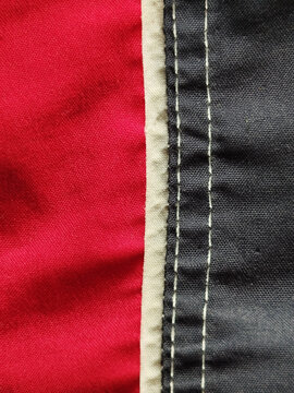 Detalle de costura con doble pespunte sobre tela t&eacute;cnica que une paneles de color rojo y gris con ribete beige