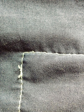 Detalle de costura con hilo claro sobre tela de sarga oscura mostrando el pespunte y la textura del tejido