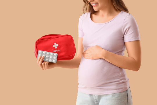 Pregnant woman holding first aid kit and pills on beige background, concept of maternity healthcare, pregnancy medication safety, prenatal care and emergency medical support