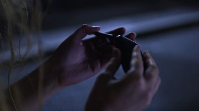 A young woman bends and flexes a flip phone in her hands at night, demonstrating its toughness and resistance to damage in a low-light urban setting. Close-up shot.