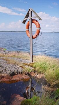 Orange lifebuoy on wooden post at rocky sea shore. Minimalist coastal safety and peaceful summer vacation concept in Nordic landscape.