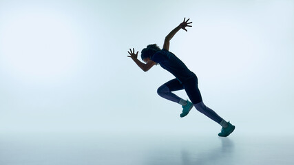 Obraz premium Teenager performing dynamic running jump in studio with clean minimal background. Concept of fitness training, active lifestyle, youth energy, and sport performance motivation.