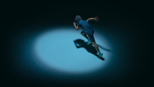 Female teenager athlete running under spotlight wearing futuristic visor in dark studio. Concept of performance tracking, sport technology, speed training, and digital fitness analytics.