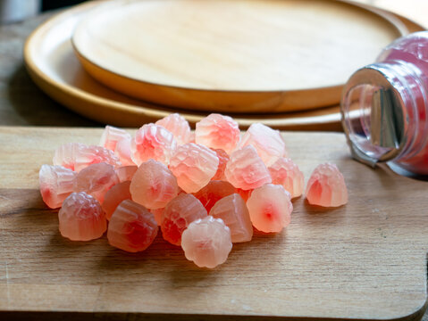 Macro close-up of translucent pink red flower-shaped health gummy vitamin supplement candy piled on wooden surface with warm bokeh
