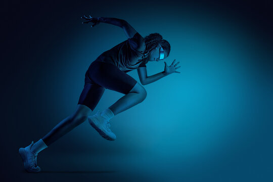 Female teenager athlete running in motion wearing futuristic visor in dark studio. Concept of augmented reality fitness analytics wearable tracking and digital performance monitoring.