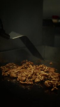 Close-up of chicken meat being cooked and stirred on a hot pan with spatula. Sizzling food and high heat cooking in professional kitchen. Steam rising and meat browning during cooking process.