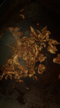 Close-up of chicken meat being cooked and stirred on a hot pan with spatula. Sizzling food and high heat cooking in professional kitchen. Steam rising and meat browning during cooking process.
