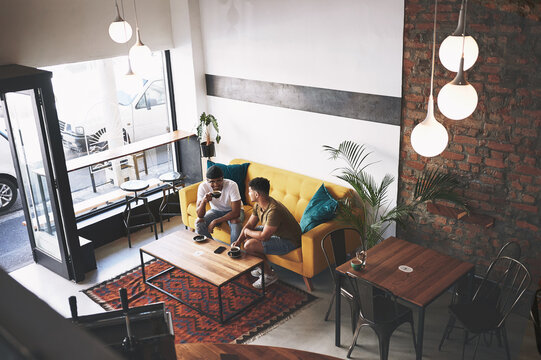 Men, friends and relax with drinks at coffee shop for conversation, bonding and above on sofa in diner. People, discussion and chill with beverage, tea cup or smile with memory on couch at cafe