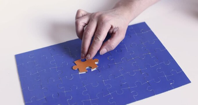 Hand placing last orange puzzle piece in blue jigsaw, completion concept, close up. Hand, puzzle piece, orange, blue, placing, last, completion, close up