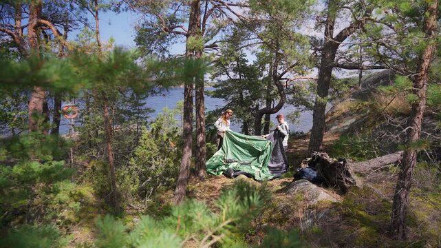 Couple setting up green tent in Finnish forest, outdoor camping scene with natural environment, focus on sustainable travel and respect for nature.