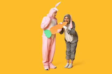 Fototapeta premium Beautiful young couple in bunny costume with paper carrot on yellow background. Easter celebration