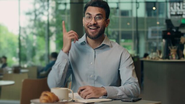 Pensive Muslim business man thinking come up with idea excited Indian Arabian businessman writing notes find answer smiling looking at camera in cafe guy executive male thoughtful think pondering