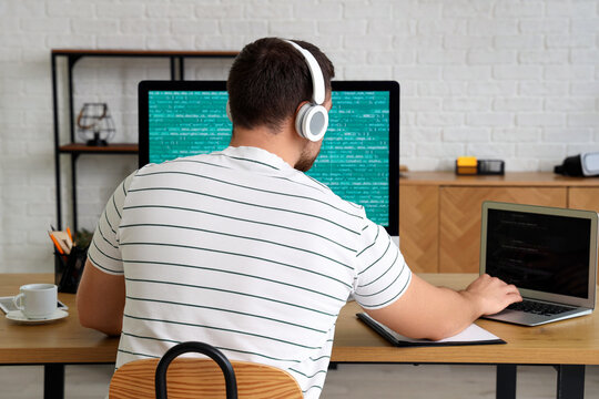 Male programmer working with computer and laptop in office, back view