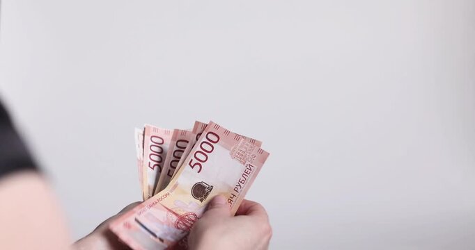 A hand fanned out to show a stack of Russian 5,000 ruble bills, soft room light