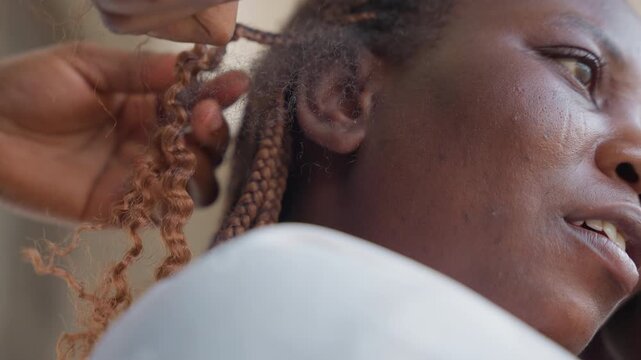 Closeup woman receiving braid near ear in quiet salon, apprentice stylist shaping textured extension with hook tool, soft natural light highlights fingers and strand detail, slow patient technique