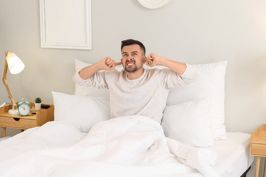 Young man suffering from loud neighbours in bedroom