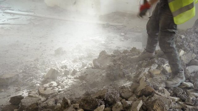 Close-up of worker breaking concrete rubble with sledgehammer in dusty ruined building. Manual labor demolition scene.