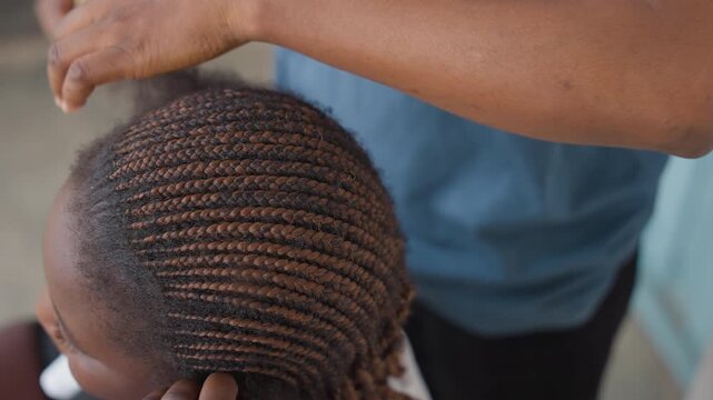 Closeup black girl cornrow braiding, hands of black stylist weaving tight rows on scalp, calm porch environment, natural light, detailed hair texture, patient careful movements, intimate family care