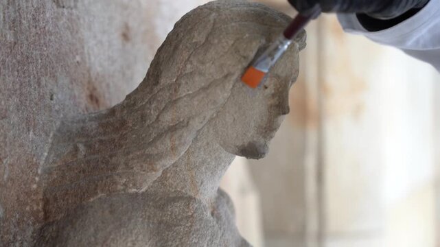 Extreme close-up of conservation specialist using a fine paint brush to meticulously clean weathering patina from a historical stone sculpture facade. Meticulous hand restoration work.