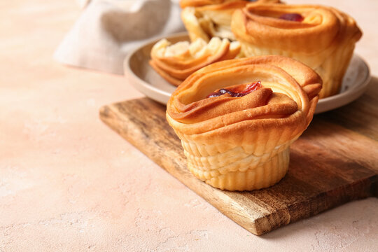 Wooden board with tasty cruffins on beige background