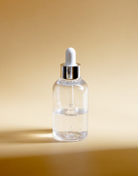 Clear glass dropper bottle with transparent serum on beige background. Cosmetic packaging mockup featuring hard shadow. Ideal for minimalist skincare marketing and dermatology brand presentation.