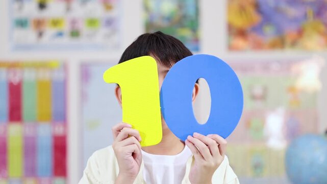 Happy Asian Boy Holding Large Number Ten Foam Cutouts in Classroom