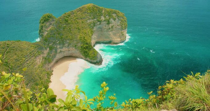 Massive rock formation shaped like dinosaur head surrounded by blue ocean at Kelingking Beach Nusa Penida Bali