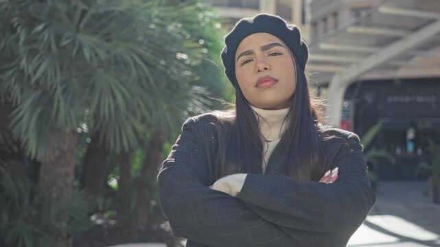 Woman with arms crossed wearing beret and coat on street, facing camera with slight tilt; quiet confidence.