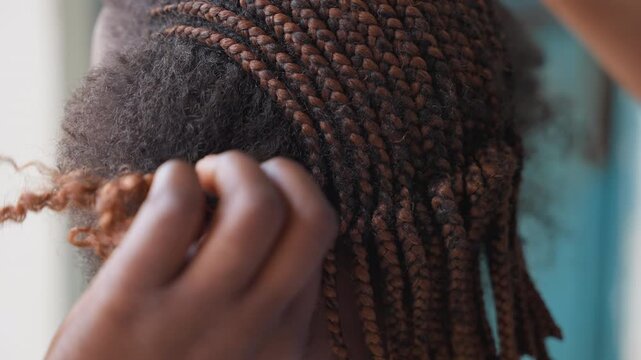 Closeup hands braiding textured hair, professional stylist working in warm studio light, fingers parting roots, adding crochet extensions and curls, careful tension and patterning, intimate slow