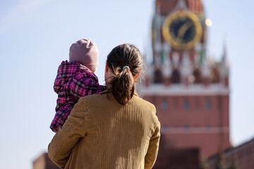 Woman with child walking on Red square on background of Kremlin tower